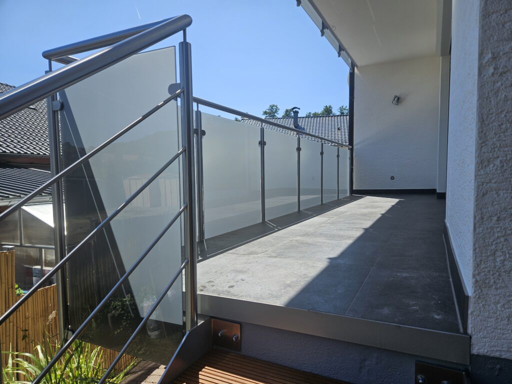 Sanierter Balkon mit grauem Bodenbelag und Edelstahl-Glasgeländer